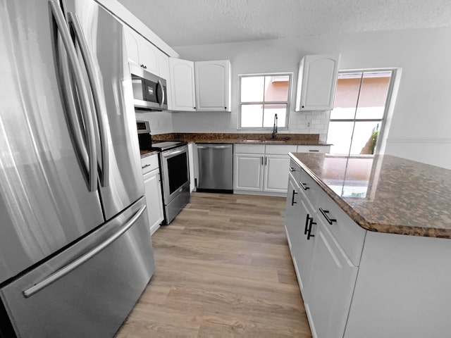 kitchen featuring a textured ceiling, appliances with stainless steel finishes, sink, light wood-type flooring, and white cabinets