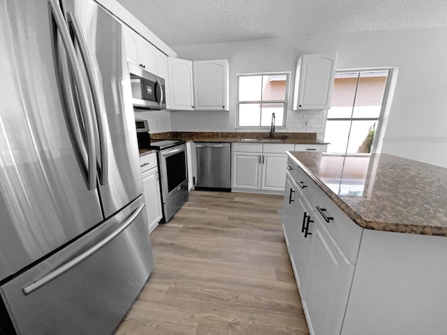 kitchen featuring light wood-type flooring, a sink, a textured ceiling, appliances with stainless steel finishes, and white cabinets