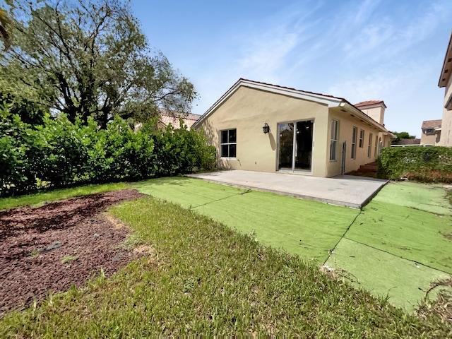 rear view of property featuring stucco siding, a patio, and a yard