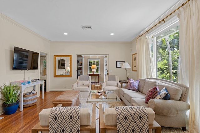 living room with wood-type flooring, ornamental molding, and a healthy amount of sunlight