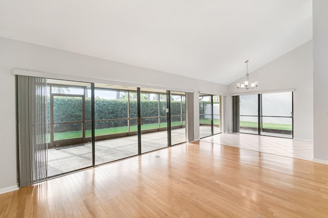 unfurnished room with high vaulted ceiling, a chandelier, and light hardwood / wood-style floors