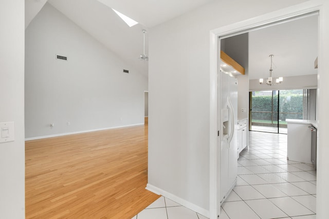 hallway with light wood-type flooring, a skylight, high vaulted ceiling, and a chandelier