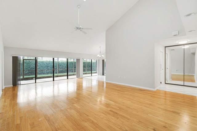 empty room with light wood-type flooring, ceiling fan with notable chandelier, and high vaulted ceiling