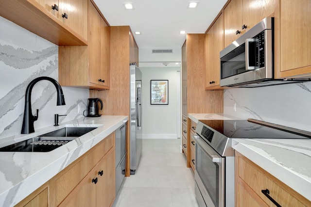 kitchen with appliances with stainless steel finishes, sink, and light stone counters