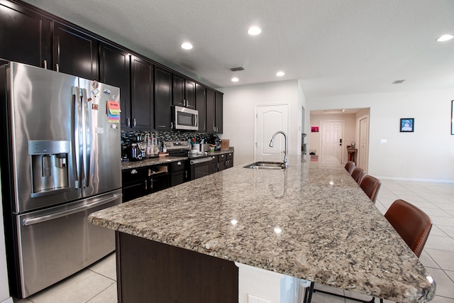 kitchen featuring appliances with stainless steel finishes, light stone countertops, sink, a large island, and a kitchen bar