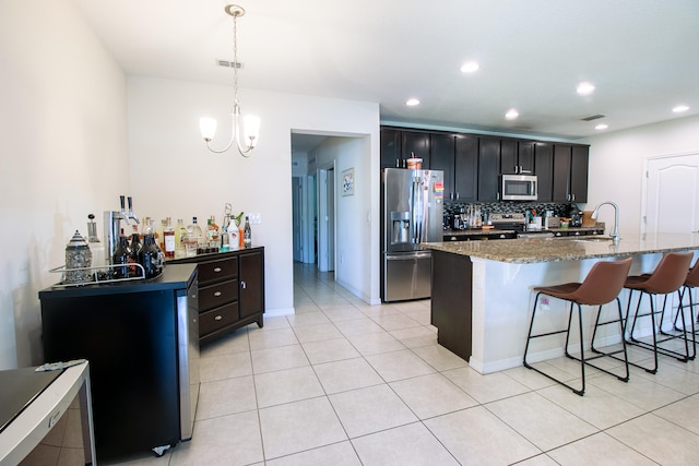 kitchen featuring decorative light fixtures, stainless steel appliances, decorative backsplash, and a center island with sink