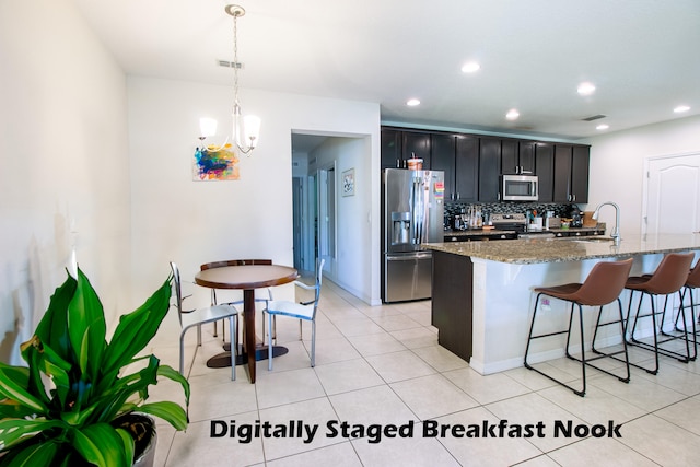 kitchen with decorative light fixtures, light stone countertops, an island with sink, a breakfast bar, and stainless steel appliances