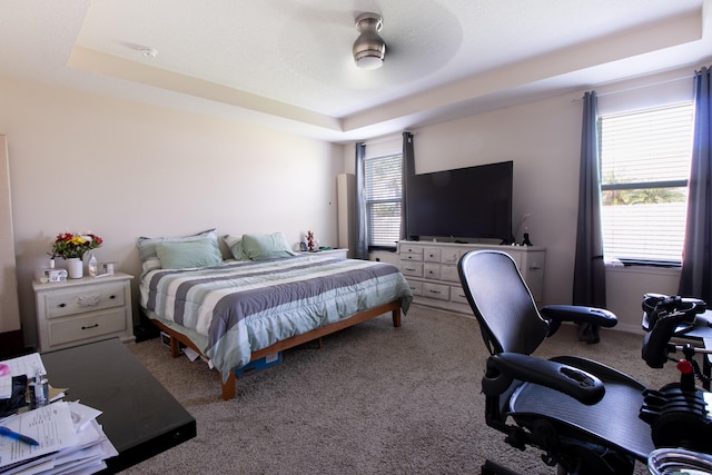 carpeted bedroom with ceiling fan and a tray ceiling