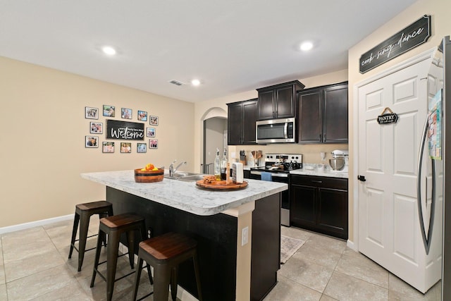 kitchen featuring sink, an island with sink, a breakfast bar, light tile patterned floors, and appliances with stainless steel finishes