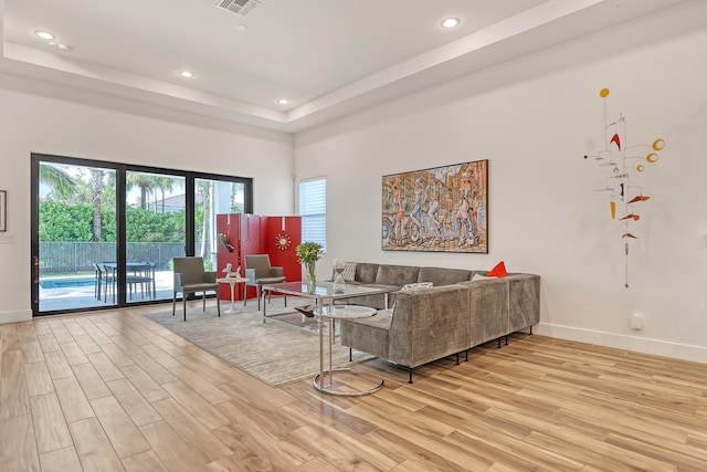 living room with light wood-type flooring and a raised ceiling