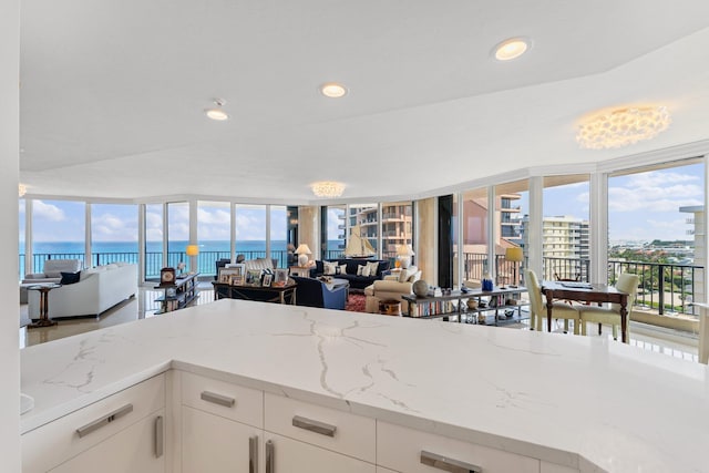 kitchen featuring white cabinetry, a water view, light stone counters, and expansive windows