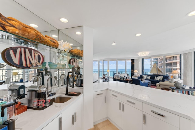 kitchen with white cabinetry, light tile patterned floors, sink, a water view, and light stone counters