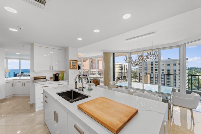 kitchen featuring white cabinetry, hanging light fixtures, sink, an island with sink, and plenty of natural light