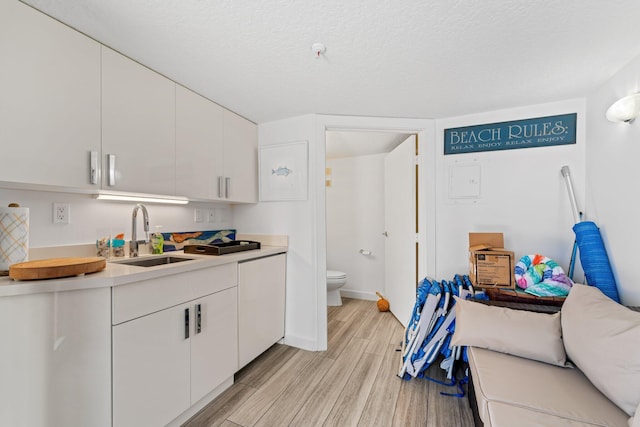 kitchen with sink, white cabinets, and light wood-type flooring