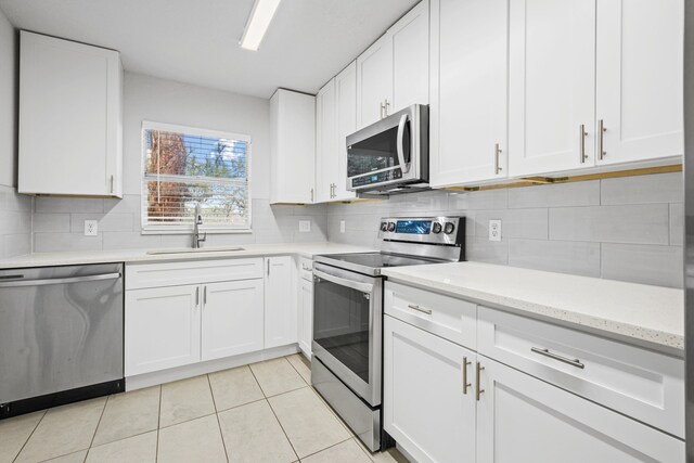 kitchen with tasteful backsplash, stainless steel appliances, sink, white cabinets, and light tile patterned flooring