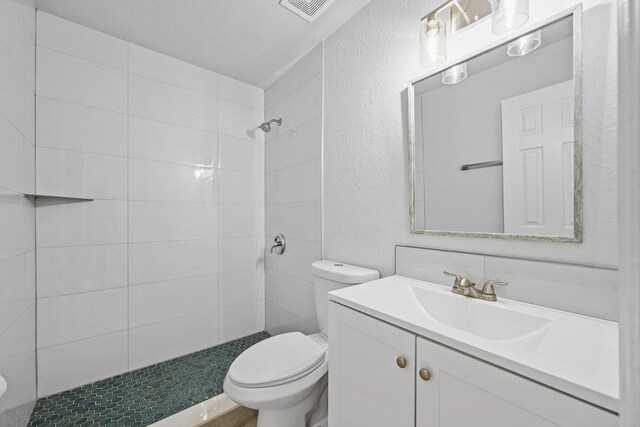 bathroom featuring tiled shower, vanity, toilet, and a textured ceiling