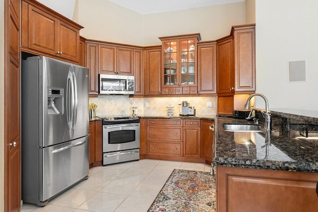 kitchen with kitchen peninsula, light tile patterned floors, stainless steel appliances, dark stone counters, and sink