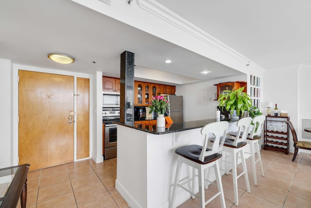 kitchen with light tile patterned floors, tasteful backsplash, appliances with stainless steel finishes, dark stone countertops, and a breakfast bar area