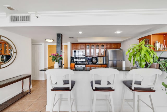 kitchen with dark stone counters, appliances with stainless steel finishes, light tile patterned floors, and a breakfast bar area