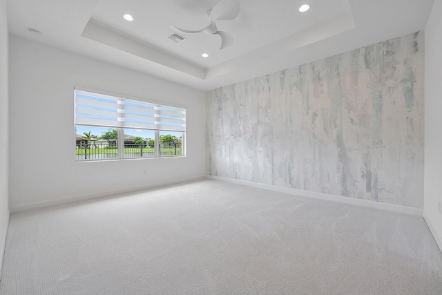 carpeted empty room with ceiling fan and a tray ceiling