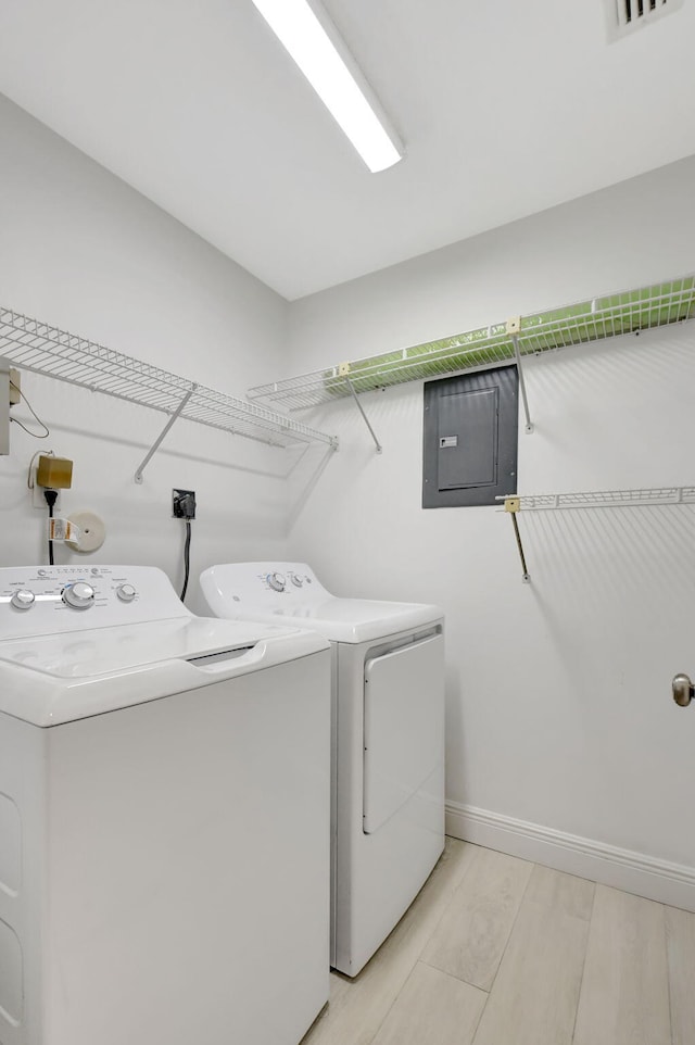 laundry area with electric panel, washer and clothes dryer, and light wood-type flooring