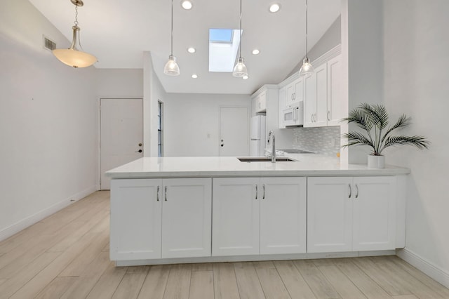 kitchen with white appliances, white cabinetry, lofted ceiling with skylight, and sink