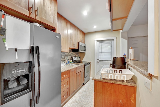 kitchen with light stone countertops, sink, backsplash, light tile patterned floors, and appliances with stainless steel finishes