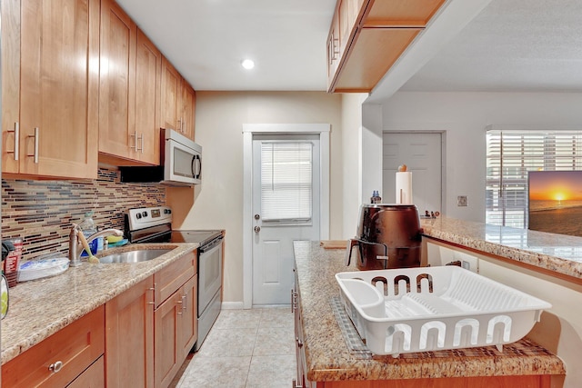 kitchen with light stone countertops, sink, tasteful backsplash, light tile patterned floors, and appliances with stainless steel finishes