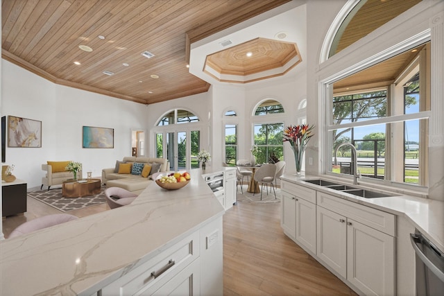 kitchen with light wood-type flooring, light stone counters, stainless steel dishwasher, wood ceiling, and white cabinets