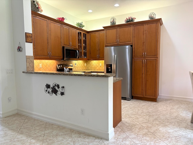 kitchen featuring appliances with stainless steel finishes, kitchen peninsula, decorative backsplash, dark stone countertops, and light tile patterned flooring