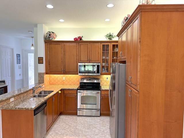 kitchen with light stone countertops, stainless steel appliances, sink, kitchen peninsula, and pendant lighting