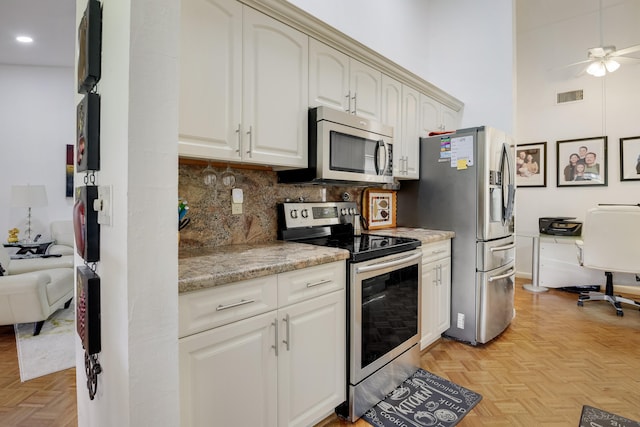 kitchen featuring decorative backsplash, light stone countertops, appliances with stainless steel finishes, and light parquet flooring