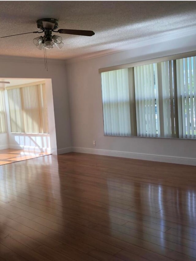 empty room with a wealth of natural light, dark wood-type flooring, ceiling fan, and a textured ceiling