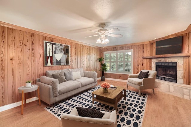 living room with ceiling fan, wood walls, hardwood / wood-style floors, a fireplace, and ornamental molding