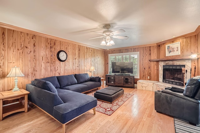 living room featuring wooden walls, ceiling fan, ornamental molding, a fireplace, and wood-type flooring