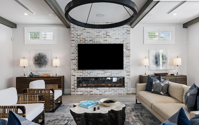 living room with beamed ceiling, wood finished floors, a large fireplace, and a healthy amount of sunlight
