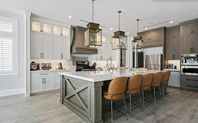 kitchen with light countertops, light wood-style flooring, stainless steel appliances, a center island with sink, and backsplash