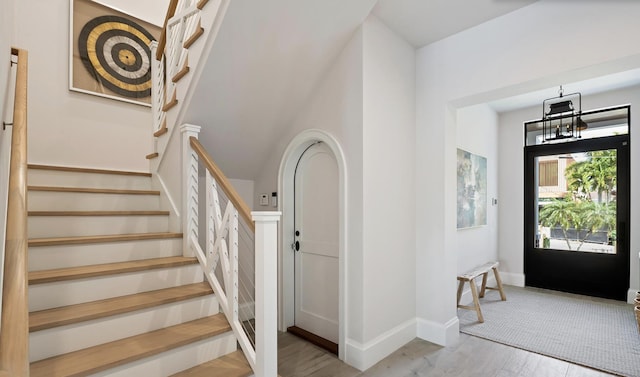 foyer entrance featuring baseboards, wood finished floors, an inviting chandelier, and stairway
