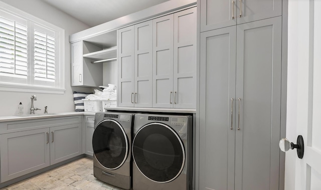 clothes washing area with washing machine and clothes dryer, cabinet space, and a sink