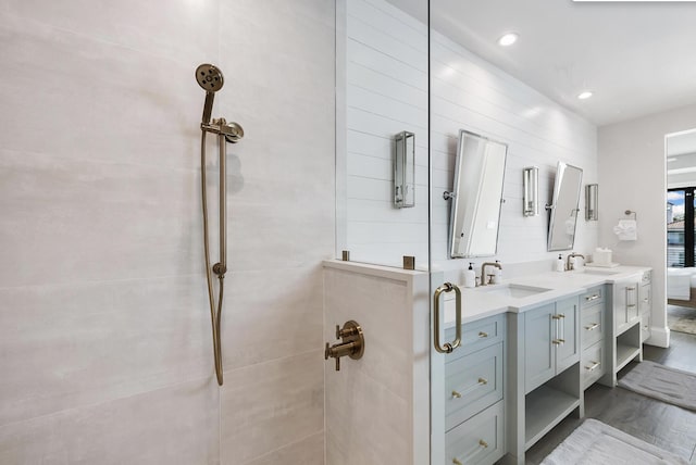 bathroom with double vanity, a sink, tiled shower, and wood finished floors