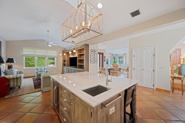 kitchen with dark tile patterned flooring, sink, ceiling fan with notable chandelier, vaulted ceiling, and a center island with sink