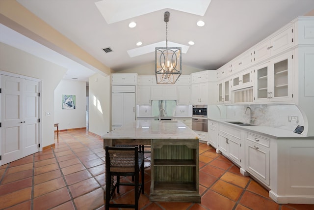 kitchen with tasteful backsplash, a kitchen island with sink, sink, white cabinetry, and paneled built in fridge