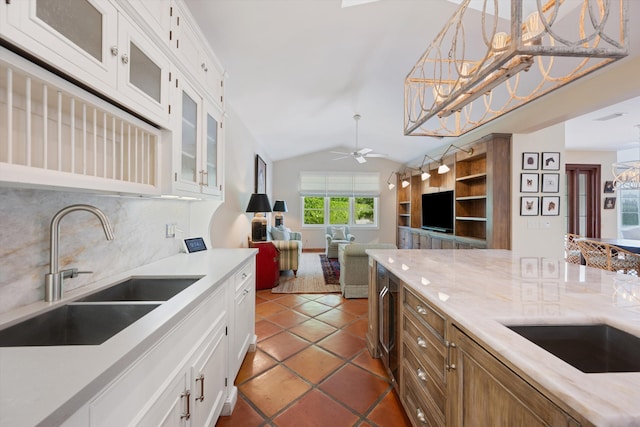 kitchen with pendant lighting, sink, backsplash, white cabinetry, and vaulted ceiling