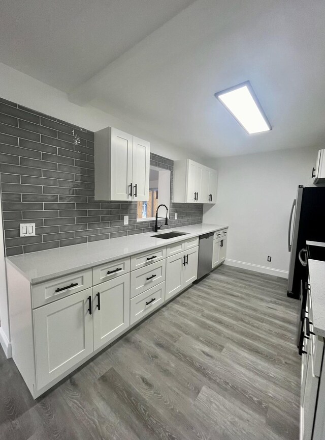 kitchen featuring wood-type flooring, sink, white cabinetry, stainless steel appliances, and decorative backsplash