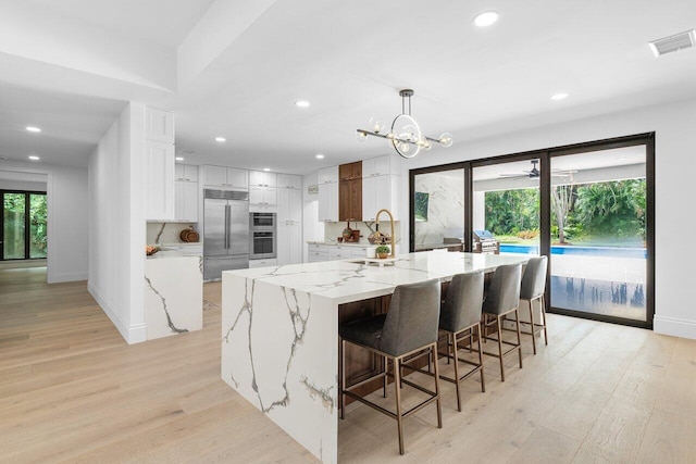 kitchen with stainless steel appliances, a large island with sink, light hardwood / wood-style floors, decorative light fixtures, and white cabinets