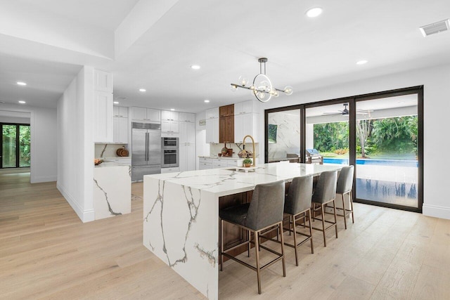 16436 Bridlewood Cir E, Delray Beach, FL 33445 - kitchen with appliances with stainless steel finishes, recessed lighting, white cabinets, light wood finished floors, and a large island with sink