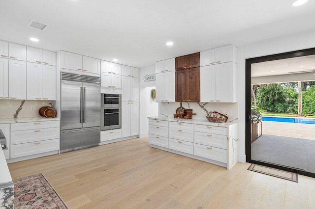 kitchen with white cabinets, appliances with stainless steel finishes, light wood-type flooring, and decorative backsplash