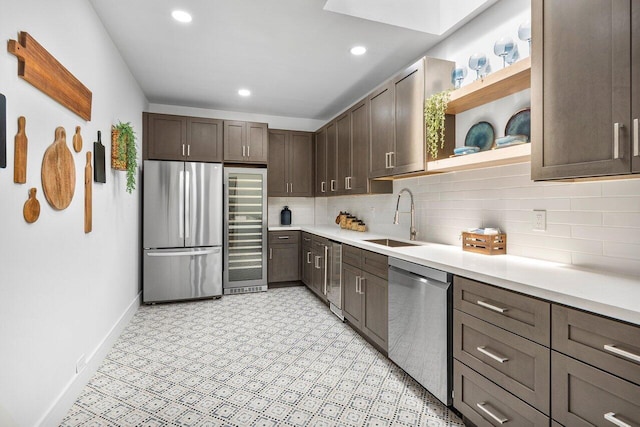 kitchen with sink, beverage cooler, backsplash, dark brown cabinets, and appliances with stainless steel finishes