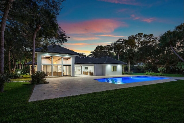 back house at dusk featuring a patio area and a yard