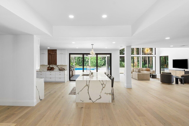 kitchen featuring white cabinets, a center island with sink, hanging light fixtures, light stone countertops, and light wood-type flooring